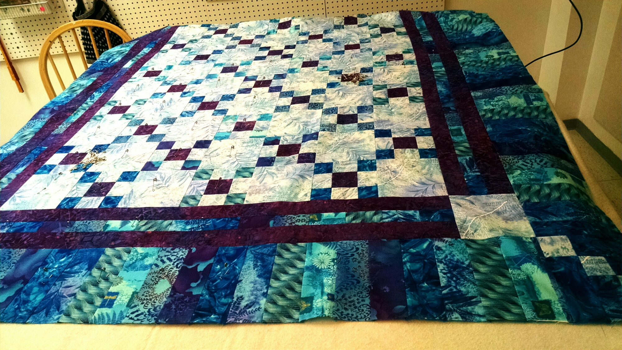 Blue and green patchwork quilt with burgundy border on a bed