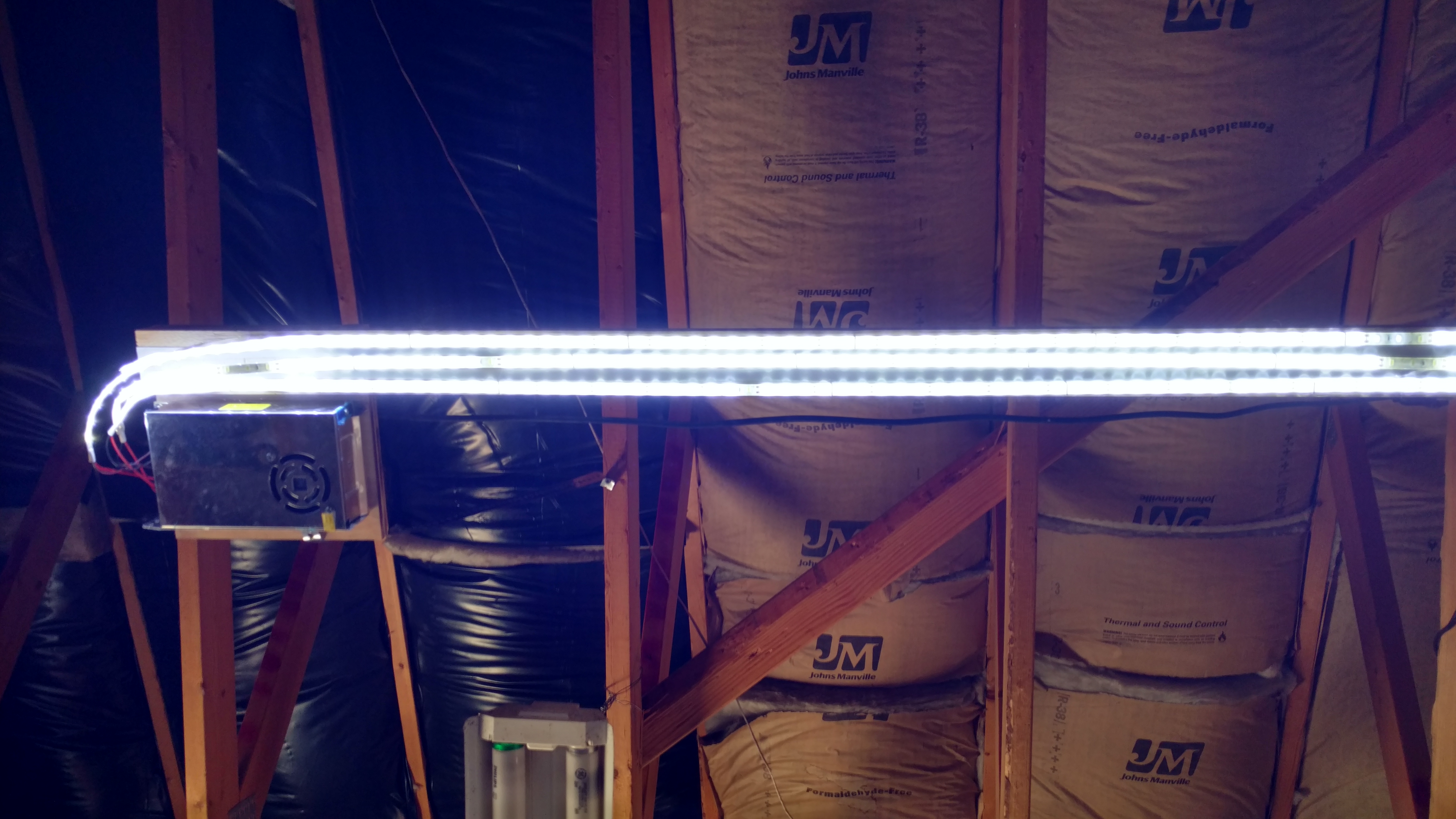 LED shop light glowing among ceiling joists and insulation