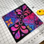 Colorful appliqued quilt block beside a rotary cutter on a cutting mat