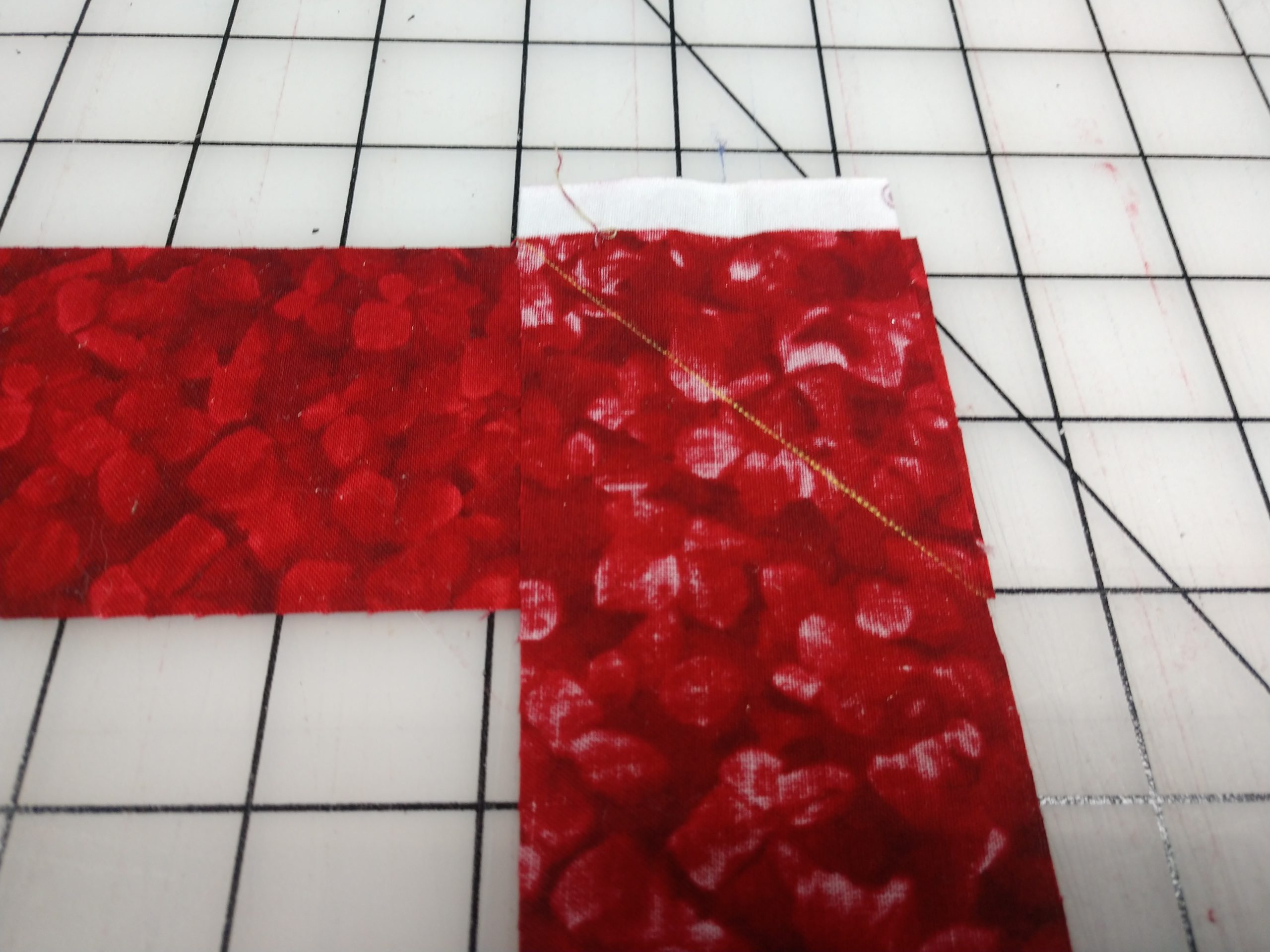 Two red binding strips joined with a diagonal seam on a cutting mat