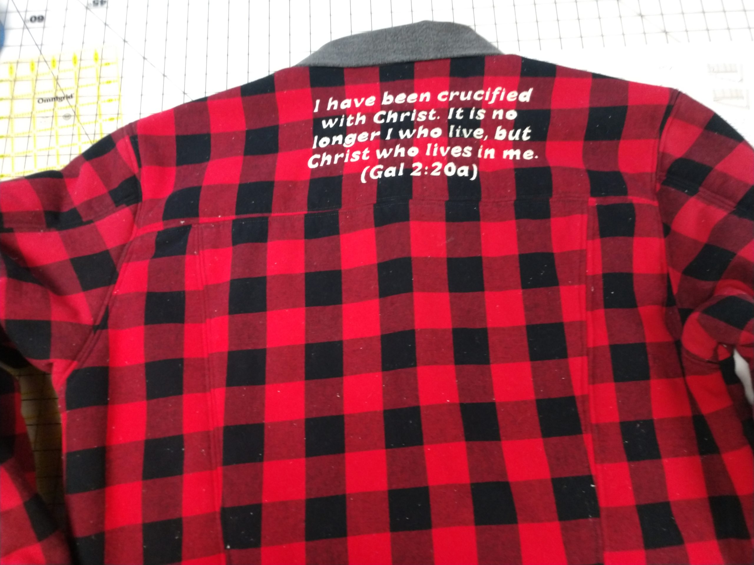 Back of buffalo plaid jacket with Galatians 2:20 verse in white lettering