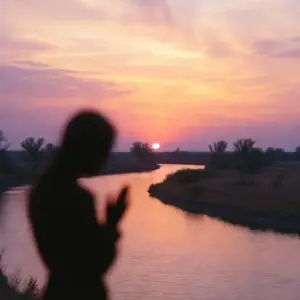 Silhouette of a woman beside a winding river at a pink and purple sunset